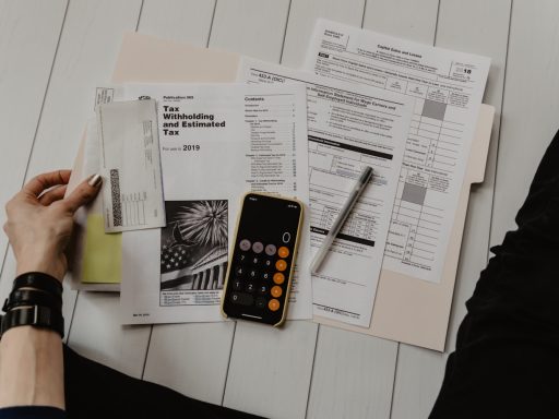 person holding paper near pen and calculator