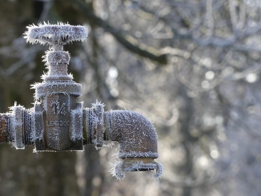 Buitenkraan met ijsvorming door vorst op een tuinmuur